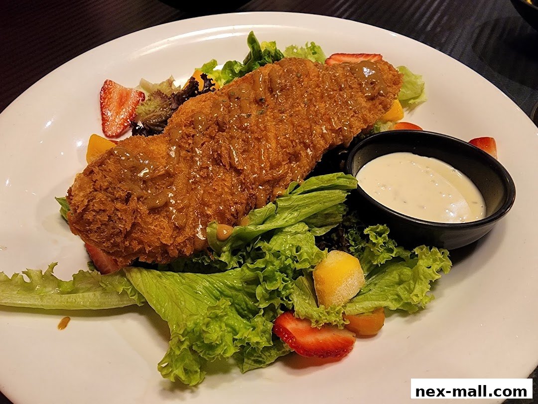 A crispy fried fish fillet served on a bed of fresh salad with strawberries and a side of dressing.