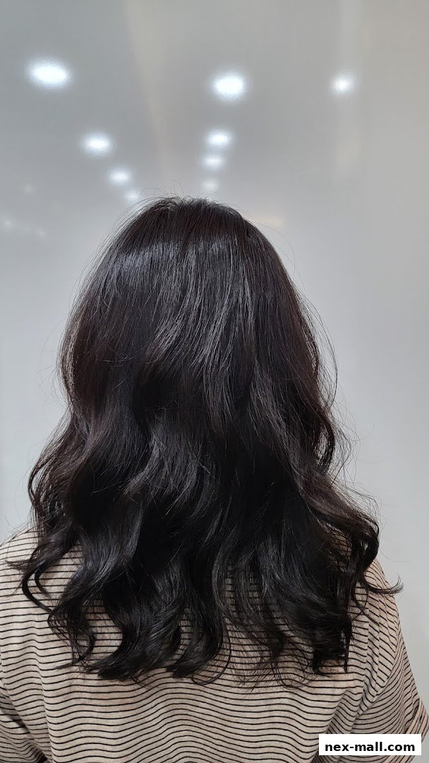 A person's back with dark, wavy hair styled and a striped shirt.