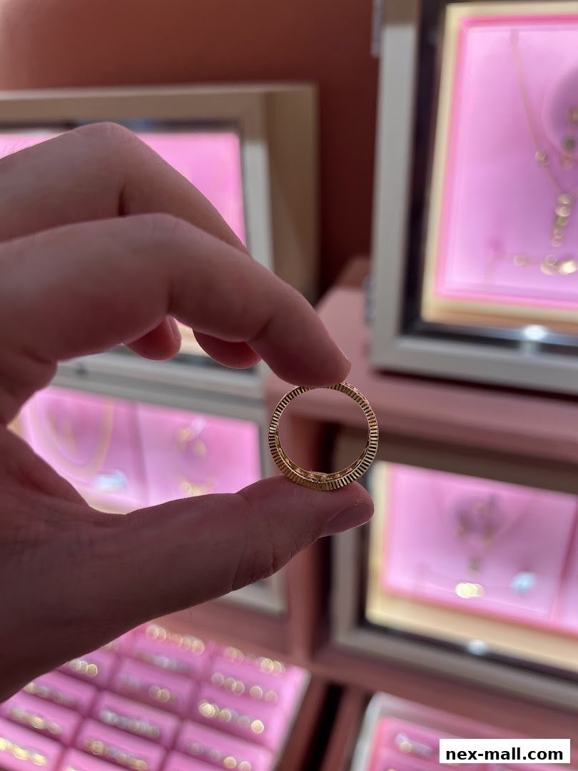 A hand holds a delicate gold ring with a textured band, showcasing jewelry displays.