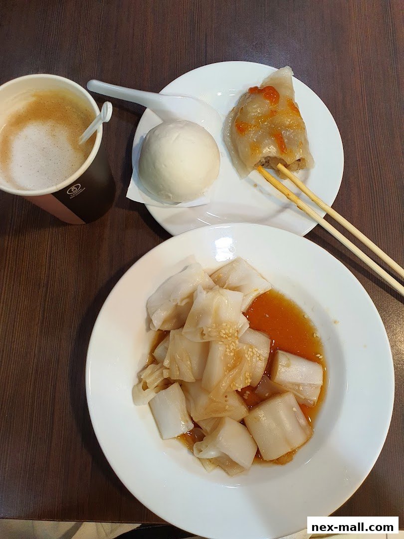 A close-up of a dim sum meal with a coffee, steamed buns, and rice noodle rolls.