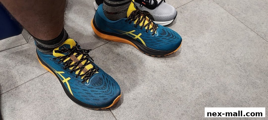 Close-up of a person wearing blue and yellow ASICS running shoes on a tiled floor.