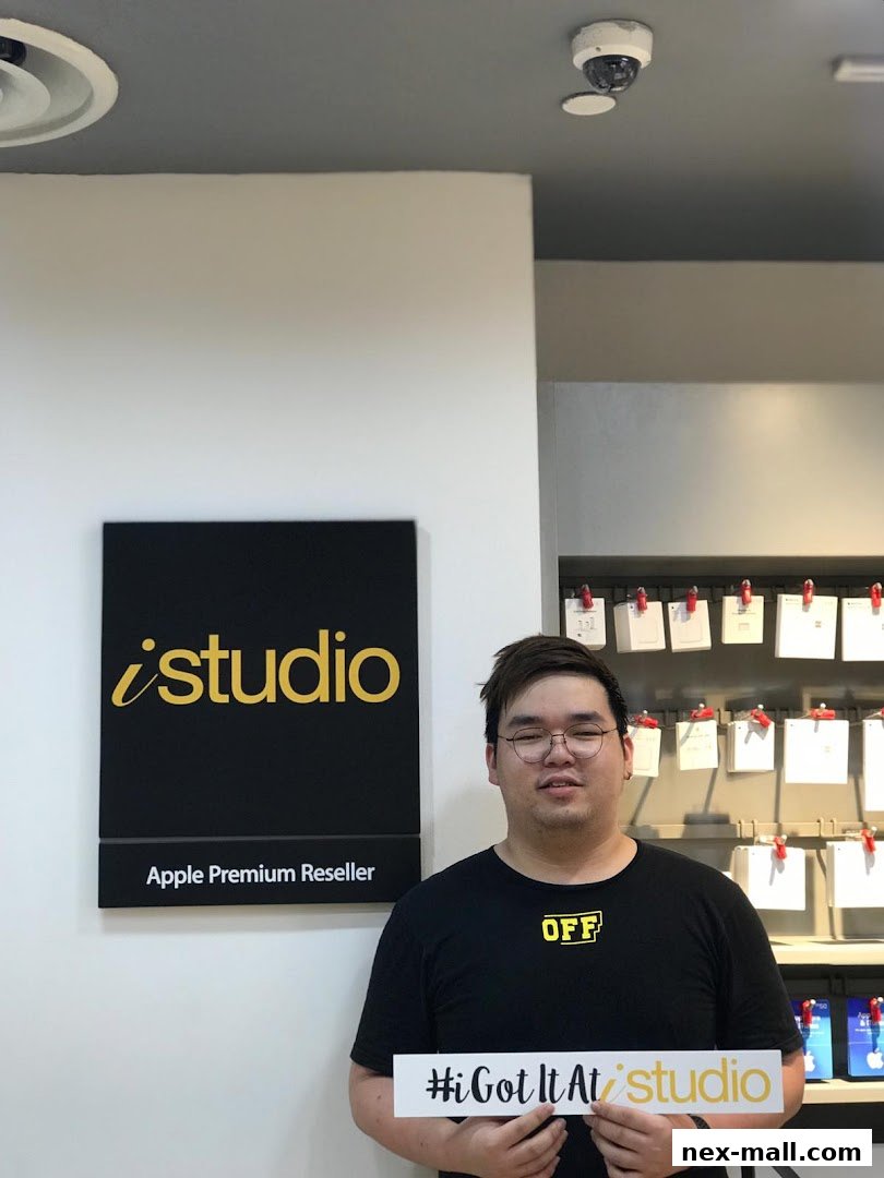 A man holds a sign in front of an iStudio Apple Premium Reseller store.