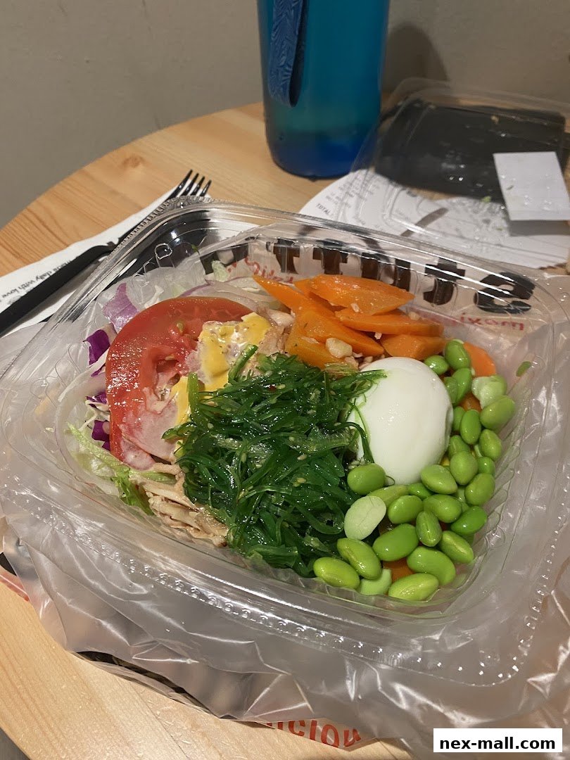 A clear plastic container filled with a colorful salad, including edamame, seaweed salad, tomato, and carrots.
