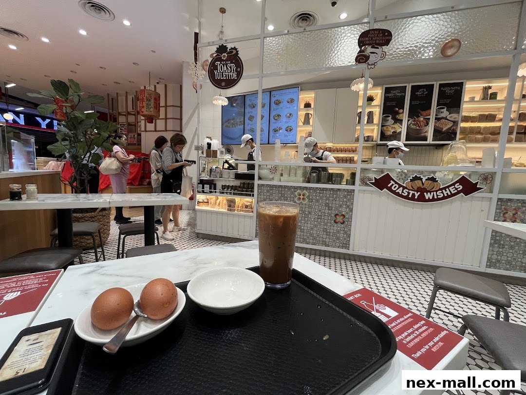 Interior view of Toast Box NEX with customers and staff, featuring food displays and seating.