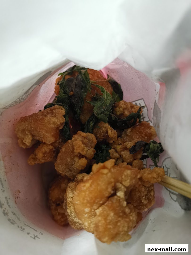 A close-up shot of crispy fried chicken pieces with basil leaves in a paper bag.