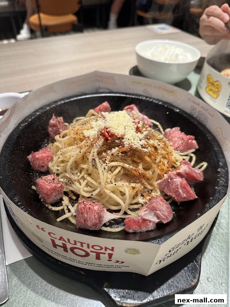 A sizzling hot plate of spaghetti with beef cubes and cheese, served with a side of rice.
