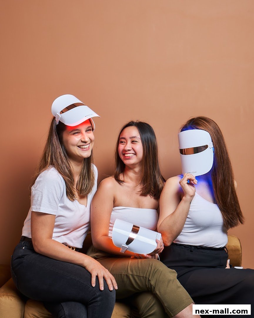 Three smiling women are sitting and holding LED therapy masks.