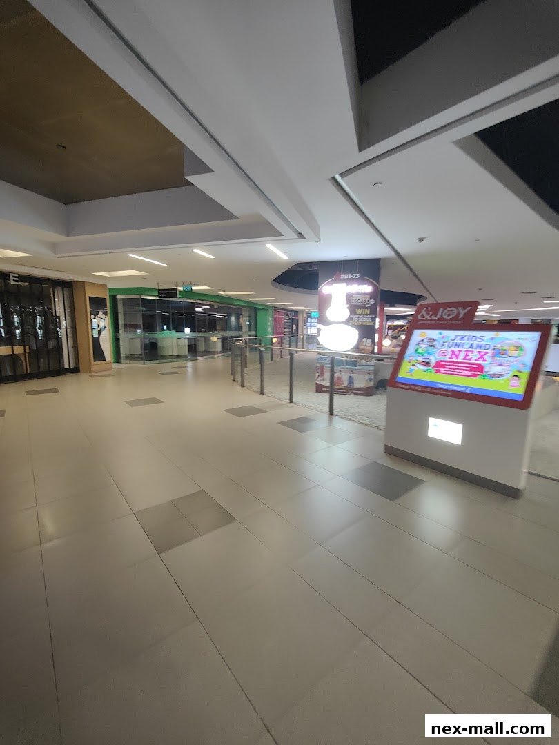 A wide shot of a shopping mall corridor with a digital display and shop entrances.