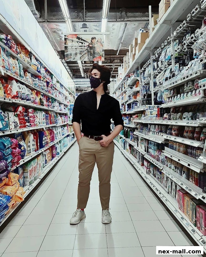 A man stands in a brightly lit supermarket aisle filled with shelves of products.