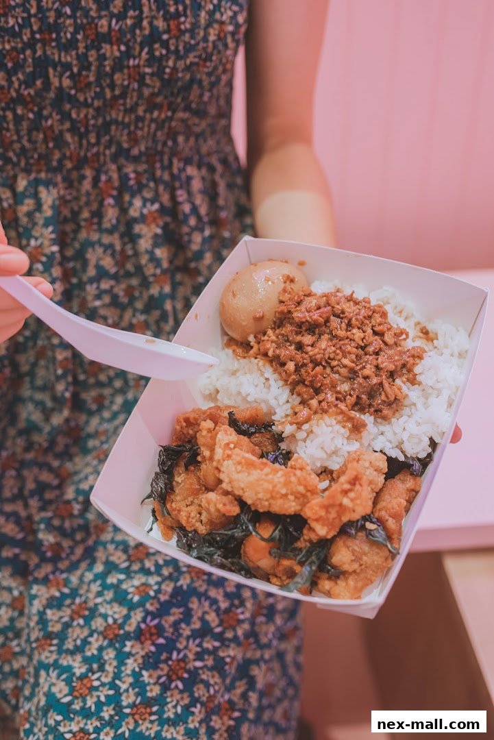 A person holds a takeout container filled with rice, braised egg, minced pork, and crispy chicken.
