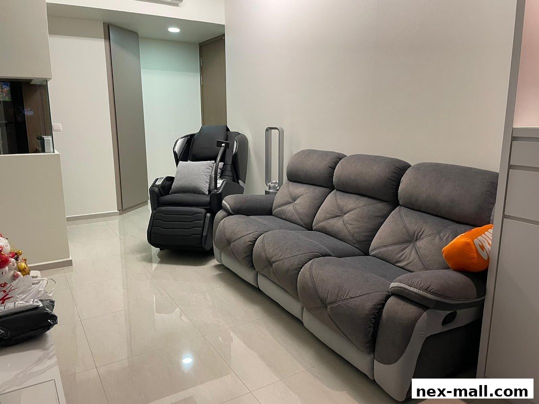 A spacious room featuring a black massage chair and a grey sofa with an orange cushion.