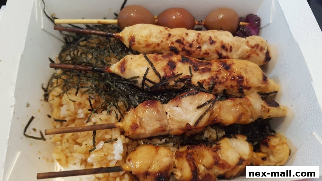 A bento box filled with grilled chicken skewers and rice, topped with seaweed.