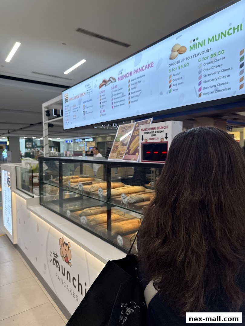 A customer stands in front of a Munchi Pancakes shop with a display of pancakes and a menu board.