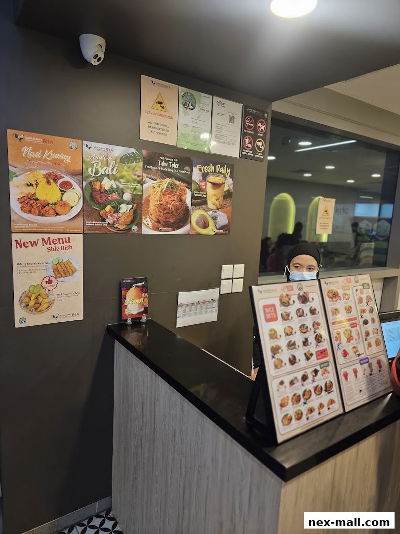 A counter at Ayam Penyet Ria with menus and a staff member wearing a mask.
