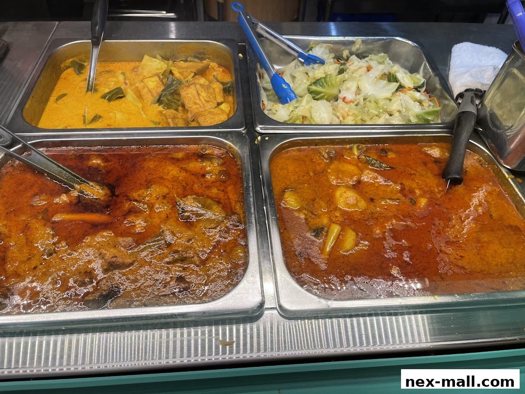 A close-up view of four metal trays filled with various curry dishes and a side of coleslaw.
