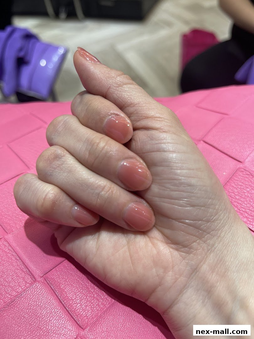 A close-up of a hand with perfectly manicured, glossy nude-toned nails.