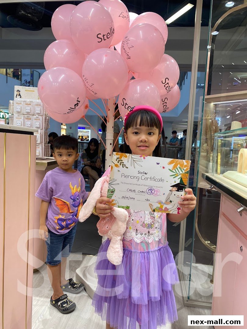 Two children pose with pink balloons and a piercing certificate at Stellar NEX.