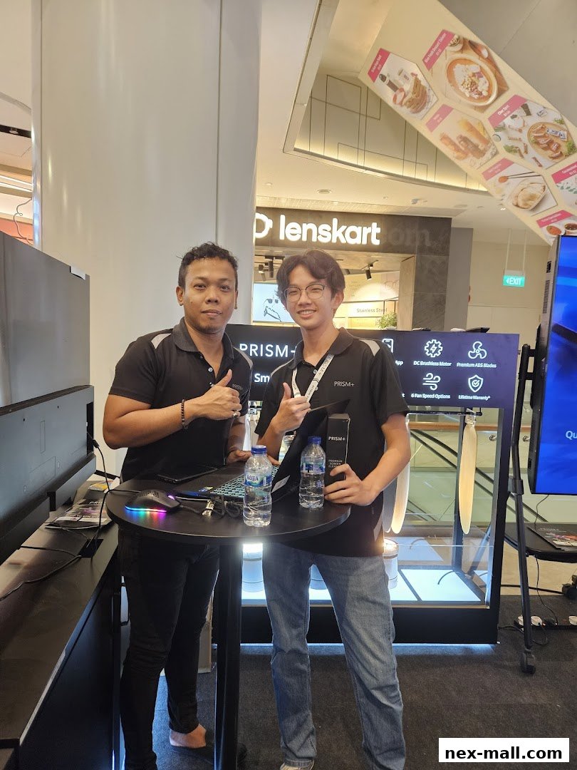 Two men stand behind a display table with products and bottles of water.