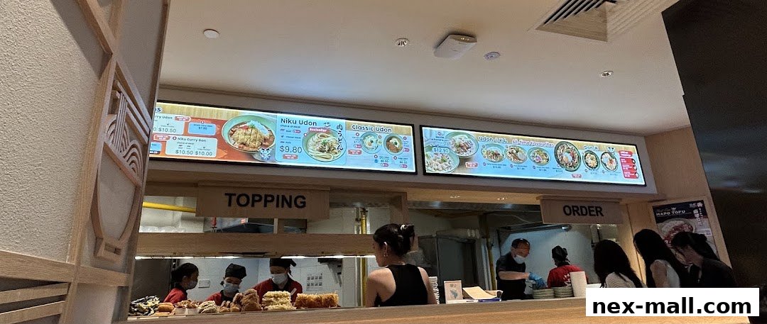 A brightly lit menu board displaying various udon dishes and prices at Idaten Udon.