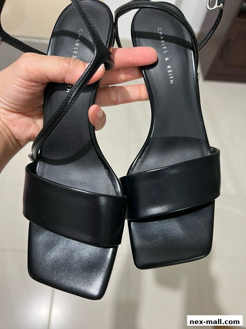 A hand holds a pair of black Charles & Keith heeled sandals.