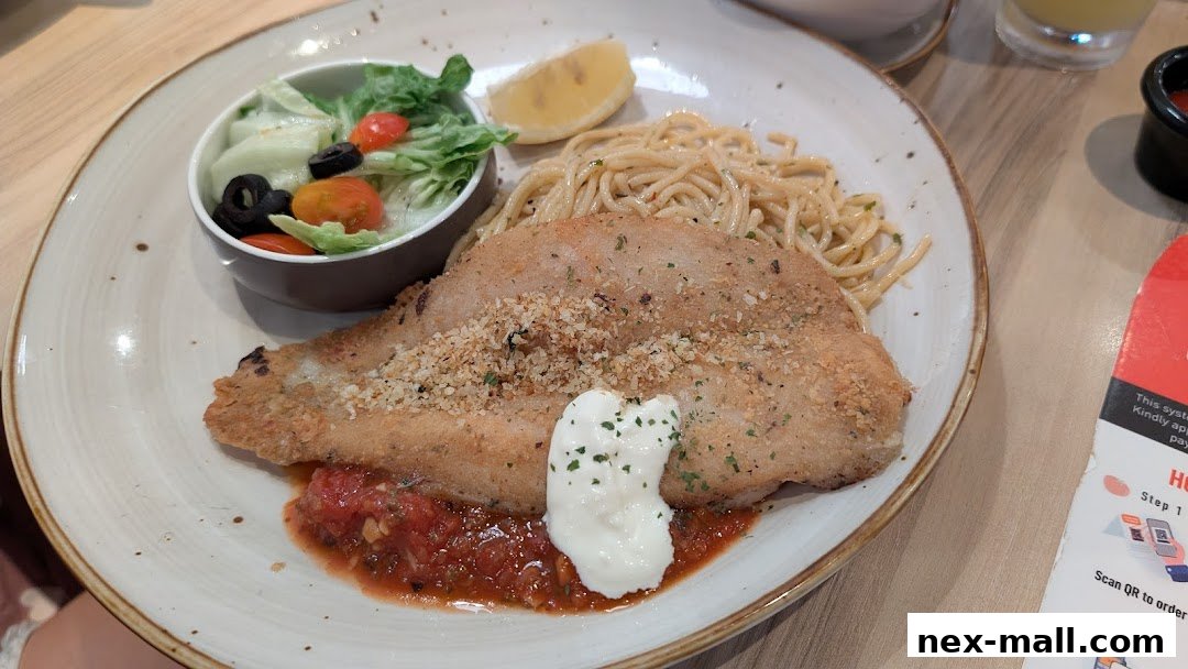 A plate of breaded fish with spaghetti, salad, and a lemon wedge.