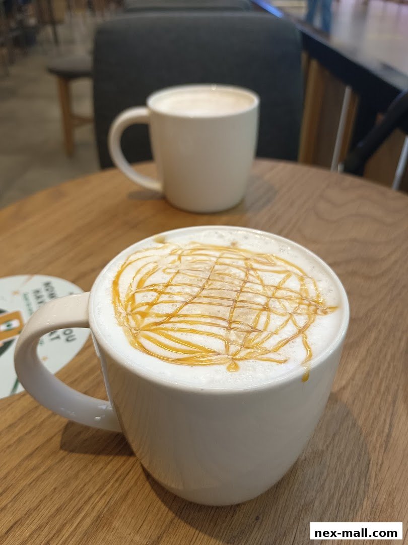 Two white mugs of coffee with caramel drizzle on a wooden table.