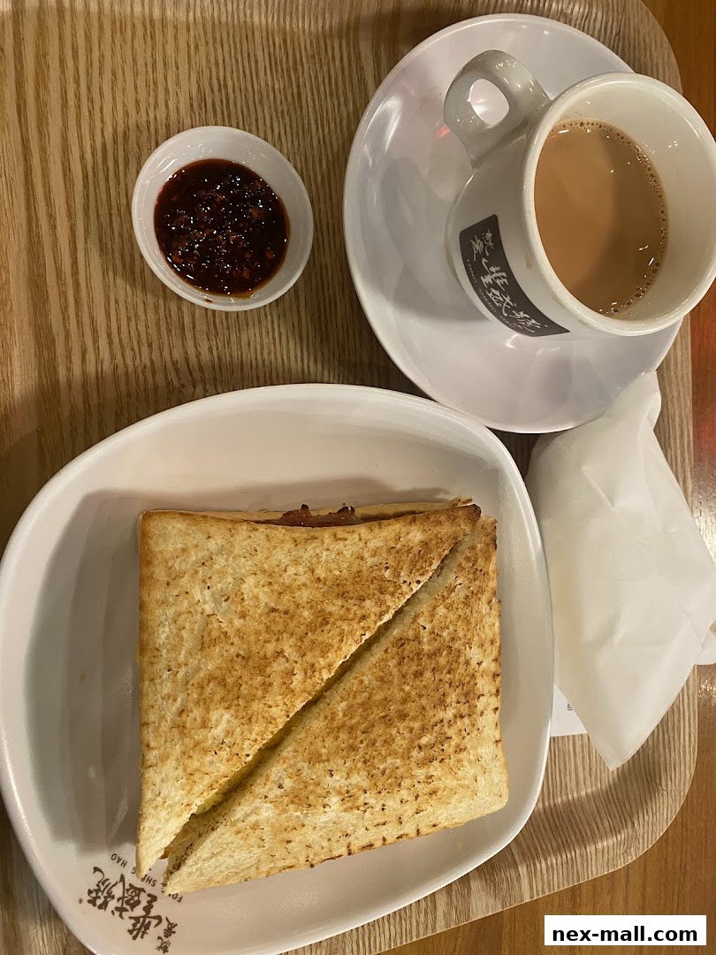 A close-up of a toasted sandwich with a side of chili sauce and a cup of milk tea.