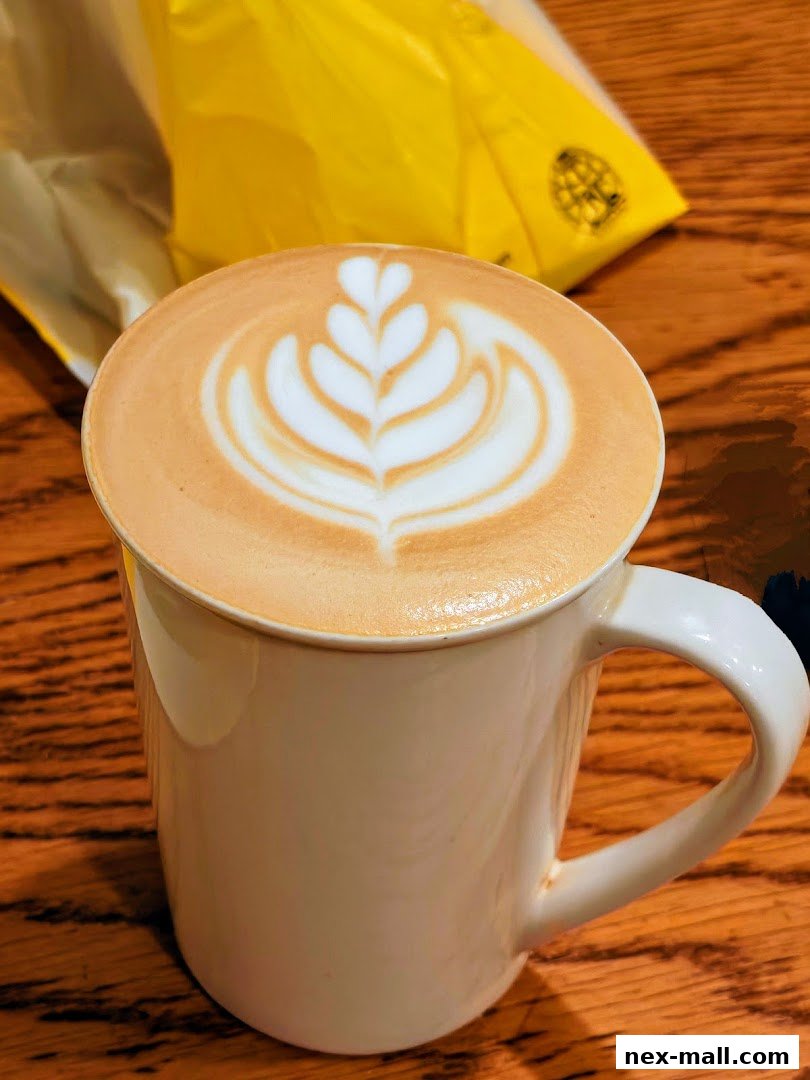 A close-up of a latte with intricate foam art in a white mug on a wooden table.