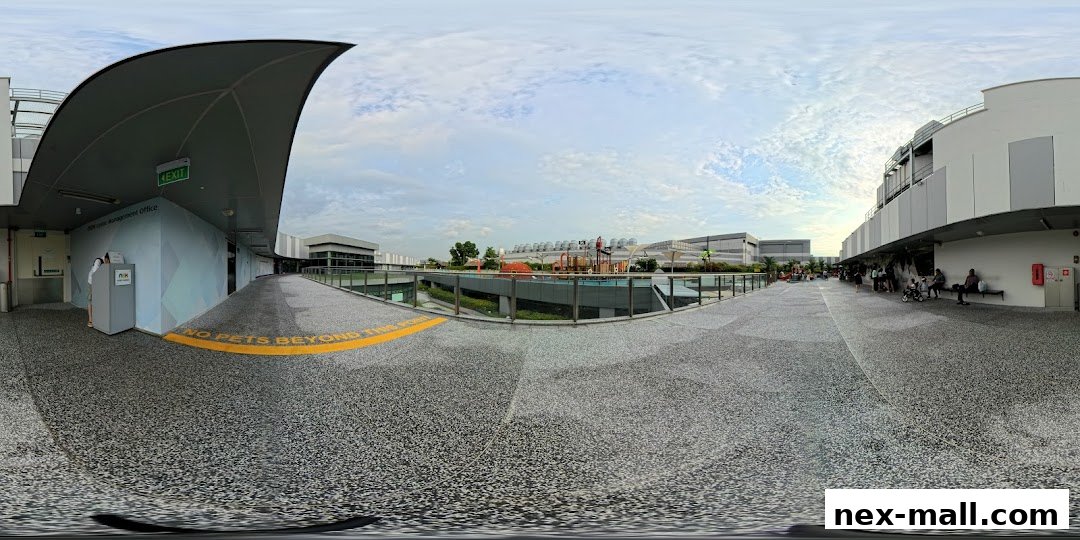 A panoramic view of an outdoor walkway with shops and a playground in the background.