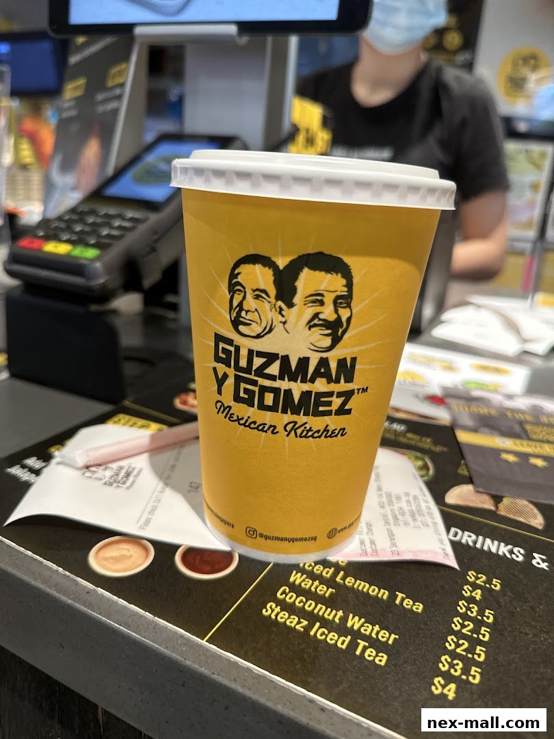 A cup from Guzman y Gomez Mexican Kitchen sits on a counter with a receipt and menu.