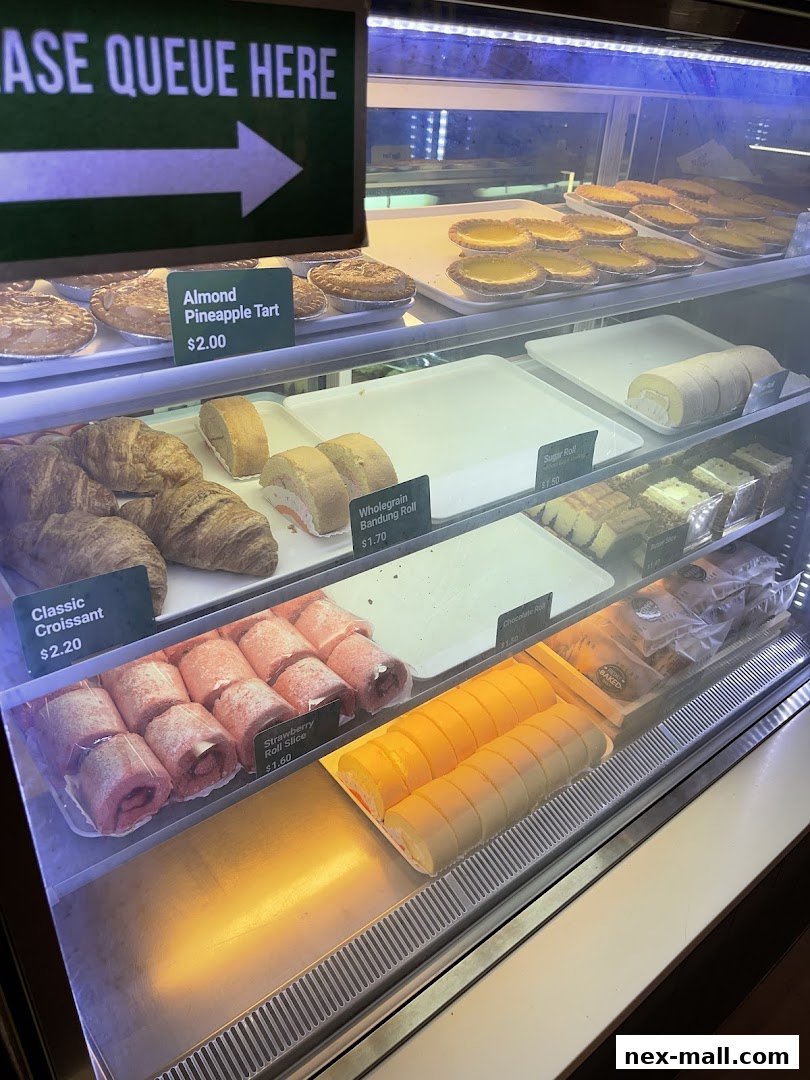 A display case filled with various pastries, including tarts, croissants, and swiss rolls.