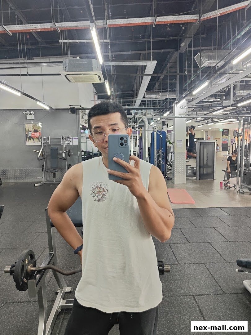 A man takes a mirror selfie in a well-equipped gym, showcasing workout equipment.