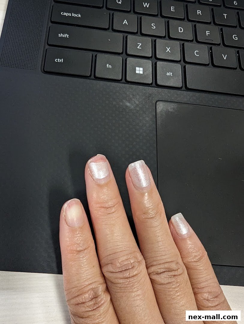 A hand with freshly painted pearlescent nails rests on a laptop keyboard.