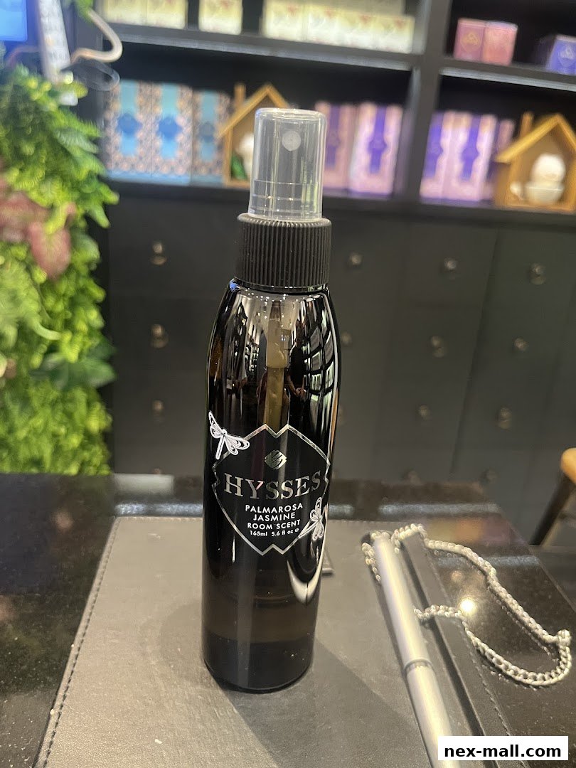 A bottle of HYSSES Palmarosa Jasmine Room Scent sits on a counter with shelves of products in the background.