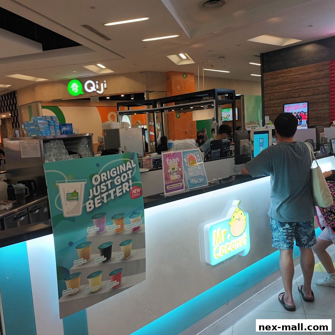A customer stands at the counter of Mr. Coconut, a beverage shop, with a menu board displaying drinks.