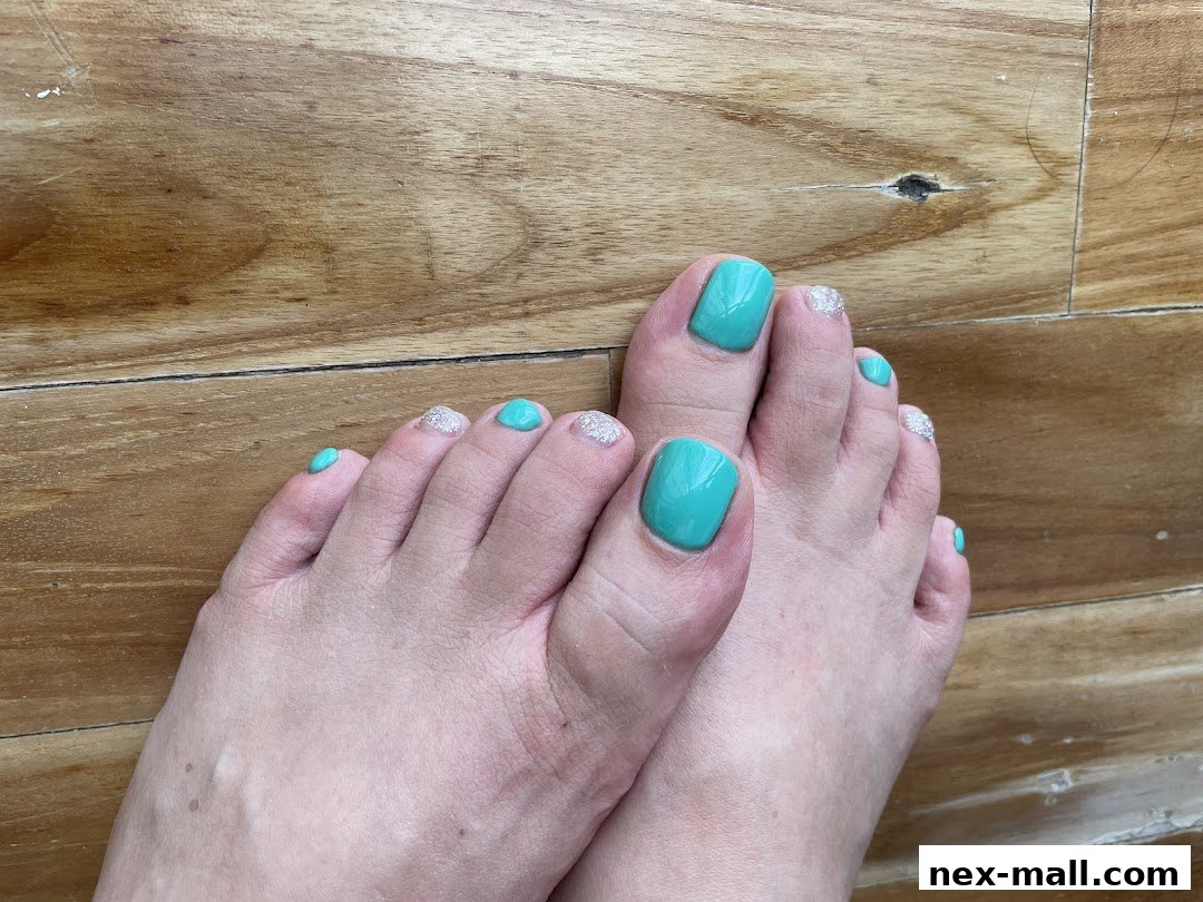 Close-up of feet with freshly painted turquoise and glitter toenails on a wooden floor.