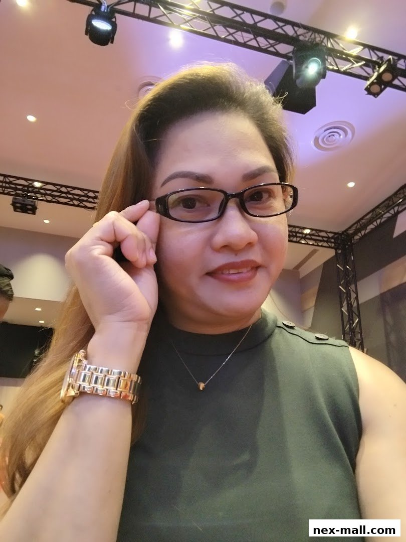 A woman wearing glasses and a green top poses for a selfie.