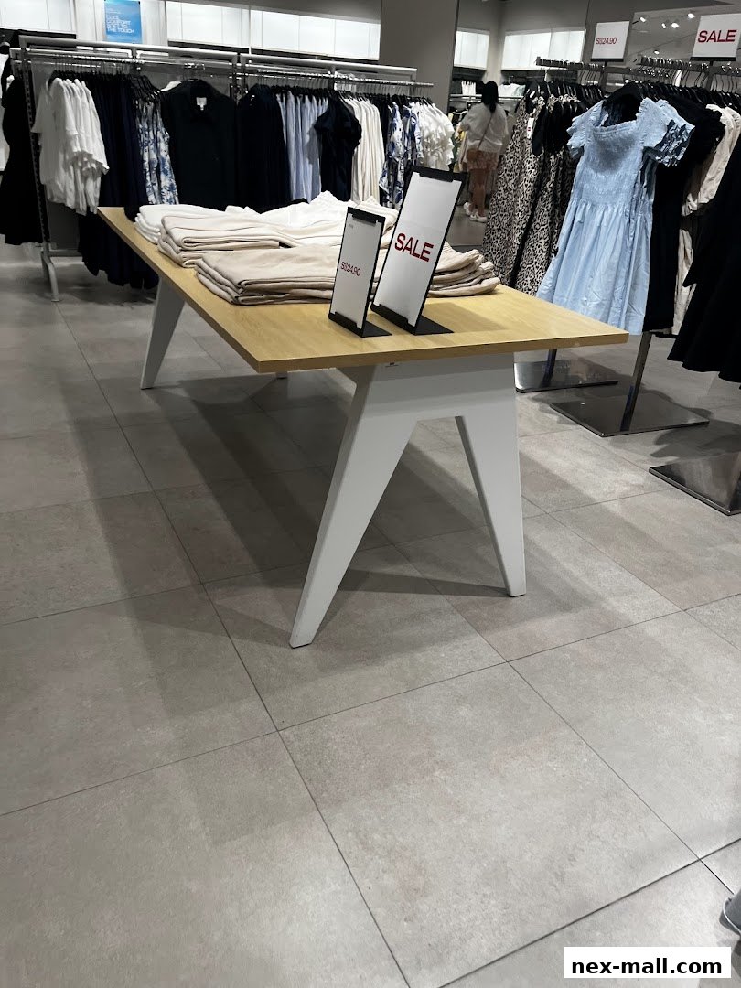 Interior view of an H&M store with clothing racks and a display table with sale signs.