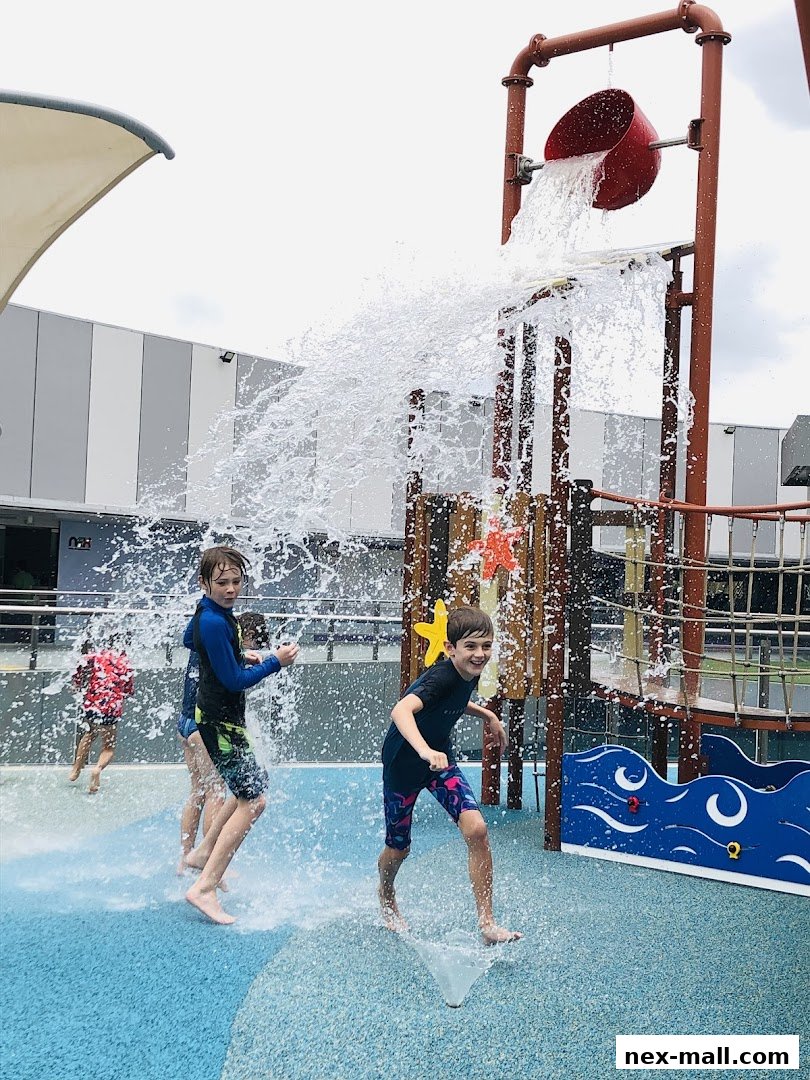 Children playing in a splash park with a tipping bucket and water jets.