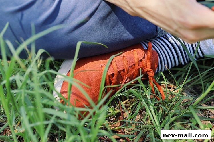 A close-up shot of a person wearing orange sneakers and striped socks, sitting in the grass.