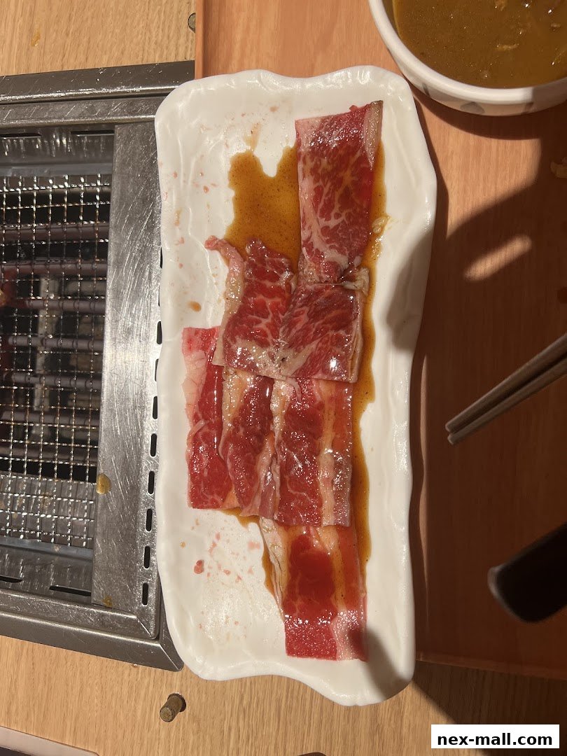 Slices of raw beef marinated in sauce on a white plate next to a grill.