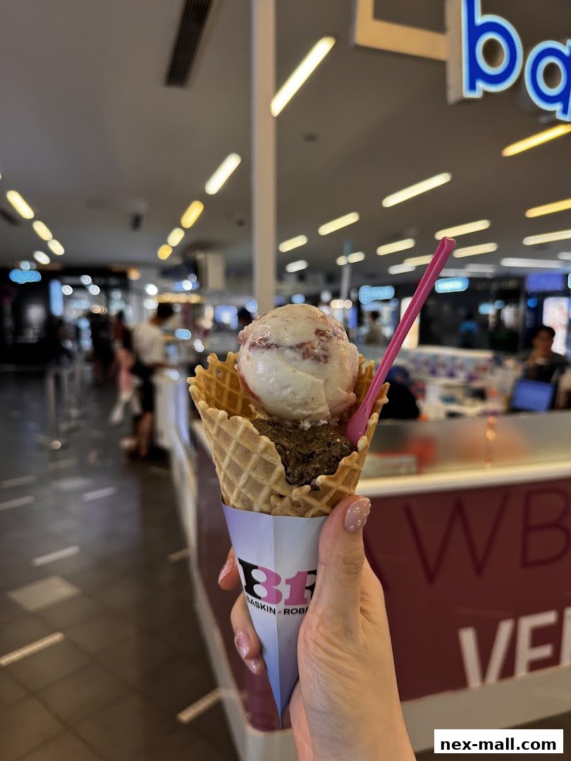 A hand holds a waffle cone with two scoops of ice cream and a pink spoon.