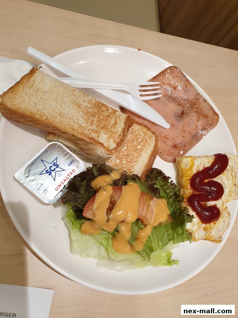 A plate of breakfast with toast, fried egg, ham, salad, and butter.