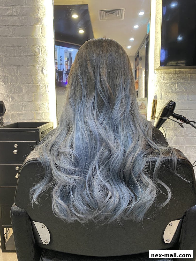 A person with long, wavy, ash-blonde and blue ombre hair sitting in a salon chair.