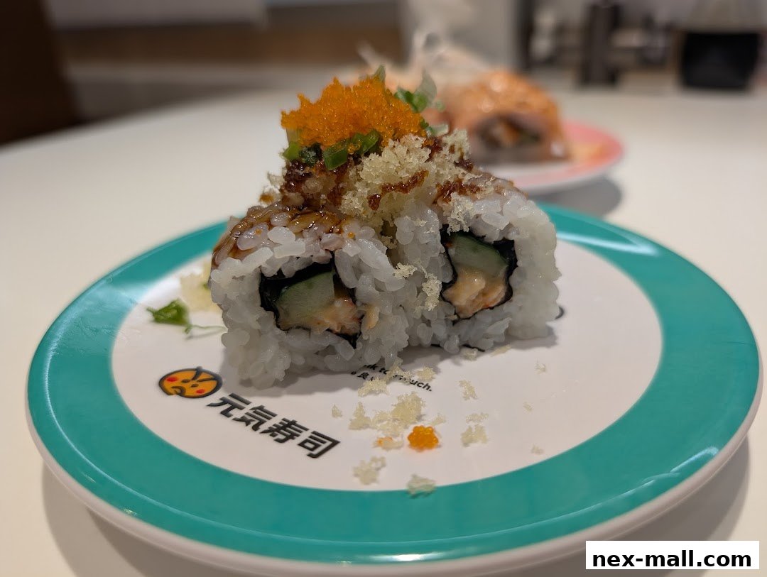 A close-up of a sushi roll with toppings on a plate with the Genki Sushi logo.