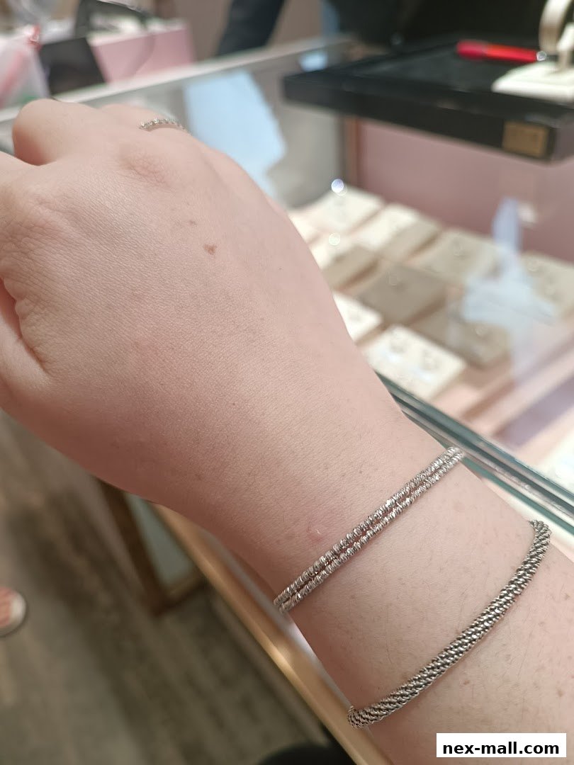 A person's wrist adorned with two delicate silver bracelets, showcasing intricate designs.