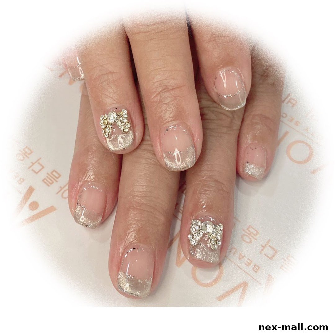 Close-up of hands with elegant French tip nails adorned with glitter and bow-shaped rhinestones.