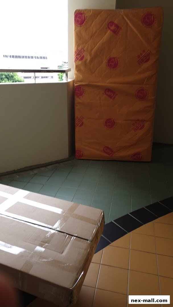 Two large items, one a mattress wrapped in orange plastic, the other a cardboard box, are on a tiled floor.