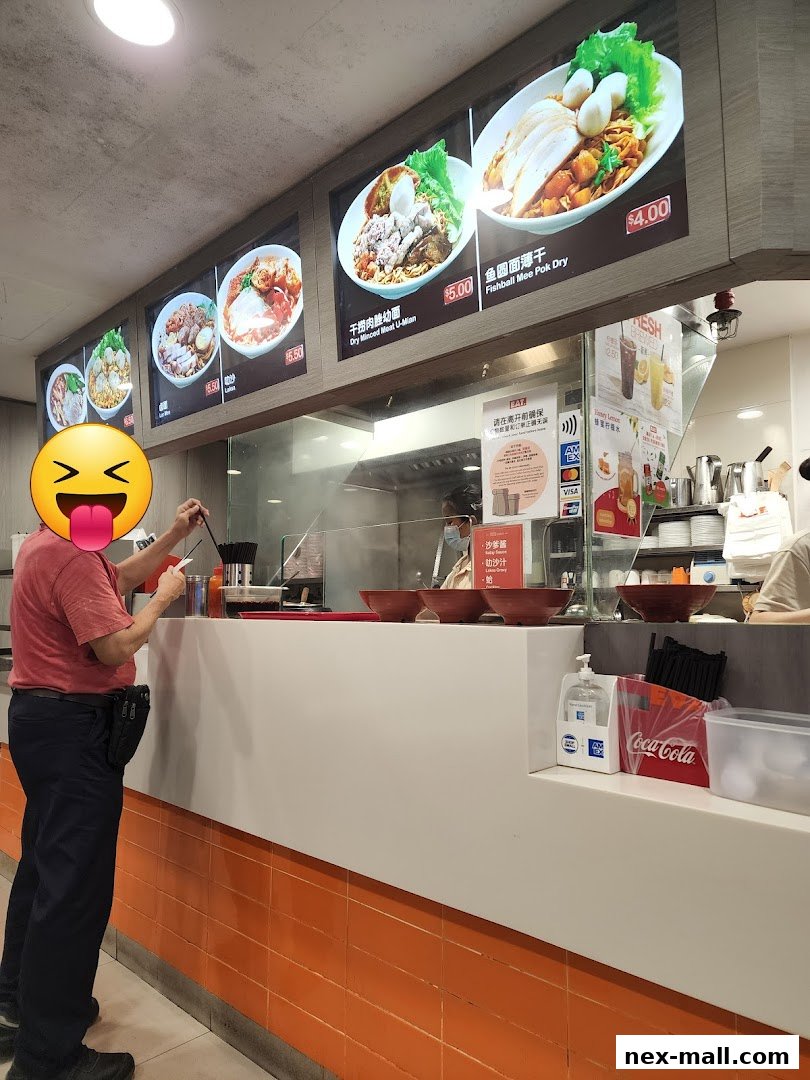 A customer orders food at a counter with illuminated menu displays showing noodle dishes.