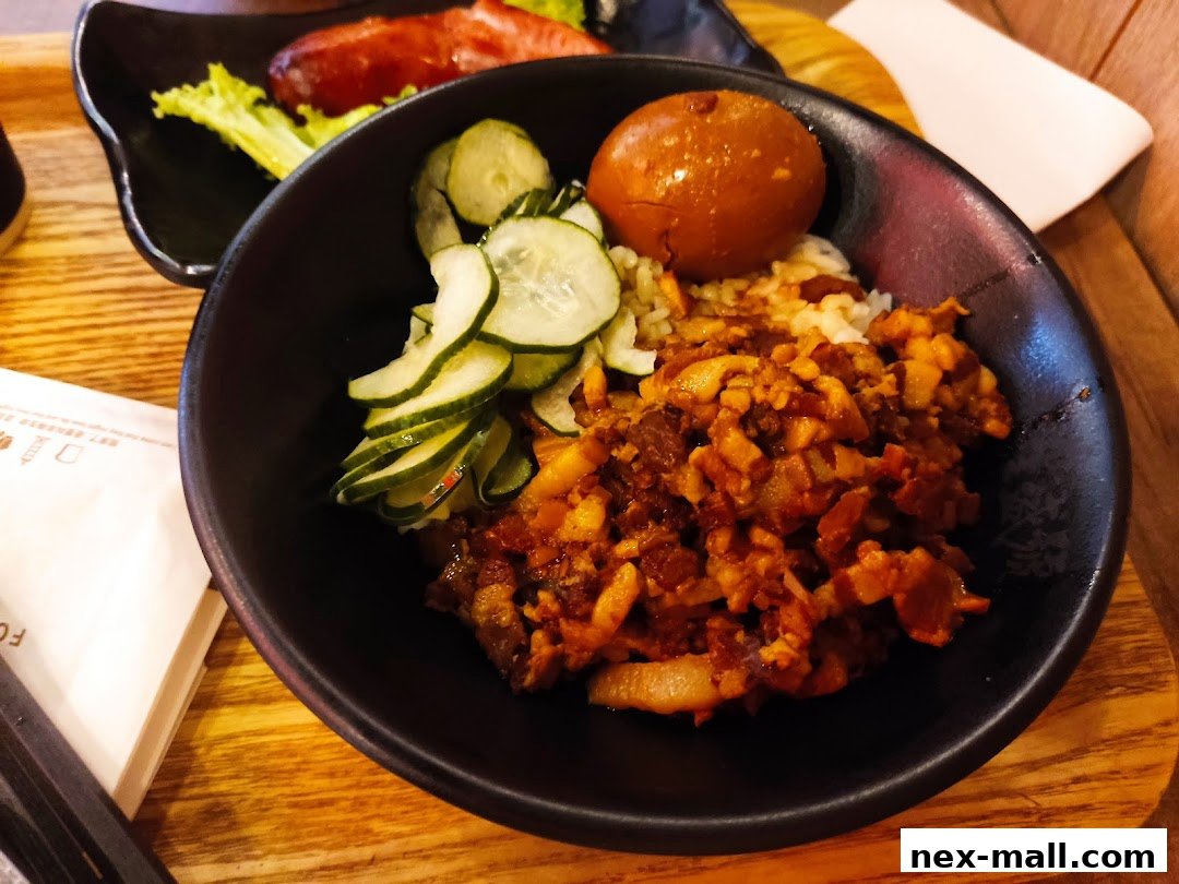 A close-up of a Taiwanese braised pork rice bowl with a braised egg and pickled cucumbers.